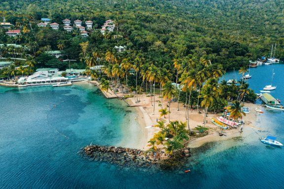 Playa rodeada de palmeras y agua cristalina, con embarcaciones en la costa.