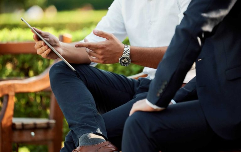 Dos personas conversando al aire libre, mostrando una tablet entre ellas.